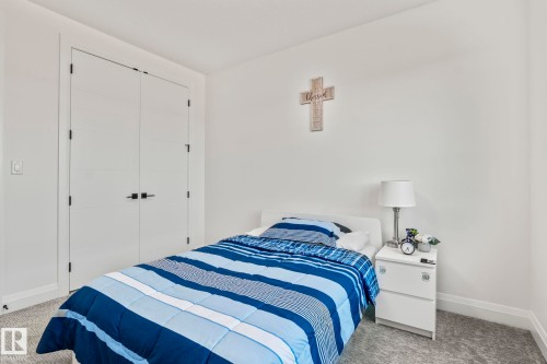 Bedroom featuring white walls, gray carpet, and white bi-fold closet doors with black hardware - 23 Elwyck Gate, Spruce Grove, AB 