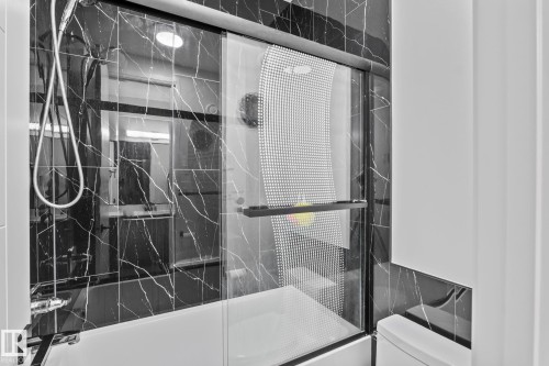 Black marble-patterned tile shower surround with white grout, featuring a sliding glass shower door with a patterned privacy film - 23 Elwyck Gate, Spruce Grove, AB 