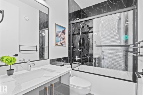 Bathroom featuring black and white patterned wall tile, a white bathtub with a sliding glass door, a vanity with an integrated sink, a chrome faucet, and a large framed mirror - 23 Elwyck Gate, Spruce Grove, AB 