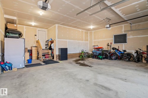 Spacious garage featuring concrete flooring, unpainted drywall, exposed ceiling joists, and overhead lighting - 23 Elwyck Gate, Spruce Grove, AB 