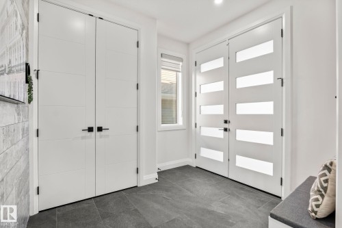 Double entry doors with frosted glass panels, dark tile flooring, a single window with blinds, and white panel doors with black hardware - 23 Elwyck Gate, Spruce Grove, AB 