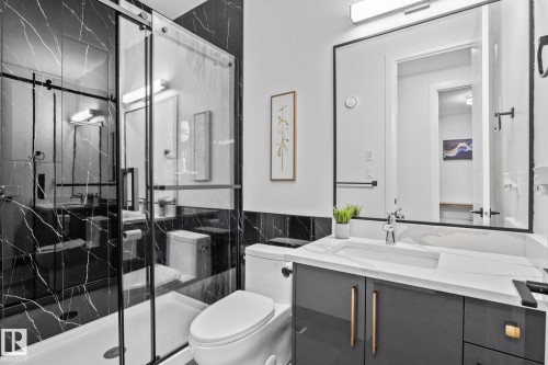 Modern bathroom featuring a glass-enclosed shower with black-veined wall tile, a white vanity with gold-tone hardware, a rectangular sink, and a framed mirror - 23 Elwyck Gate, Spruce Grove, AB 