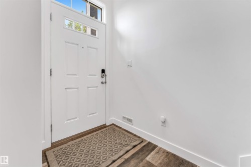 Entryway featuring a white paneled door with glass inserts, transom window, wood-finish flooring, and crisp white walls - 116 3305 Orchards Link Sw, Edmonton, AB 