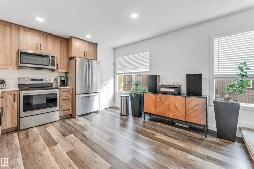 Modern kitchen featuring stainless steel appliances, light wood-finish cabinetry, crisp white countertops, and a white subway tile backsplash - 116 3305 Orchards Link Sw, Edmonton, AB 