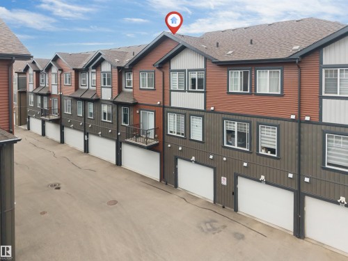 Multi-level townhome featuring a private balcony with black iron railings, a dedicated single-car garage, and a brown shingle roof - 116 3305 Orchards Link Sw, Edmonton, AB 