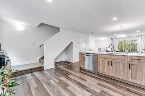 Open-concept kitchen featuring an island with light wood-finish cabinetry, a stainless steel dishwasher, and a gooseneck faucet - 116 3305 Orchards Link Sw, Edmonton, AB 