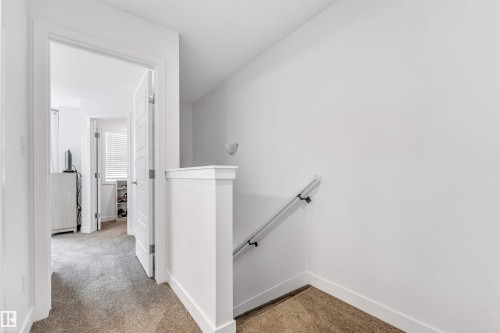 Hallway featuring plush carpeting, white walls, and a contemporary handrail leading to a lower level - 116 3305 Orchards Link Sw, Edmonton, AB 
