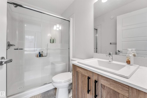 Contemporary bathroom featuring a wood-finish vanity with a white rectangular sink, a white countertop, and a chrome faucet - 116 3305 Orchards Link Sw, Edmonton, AB 