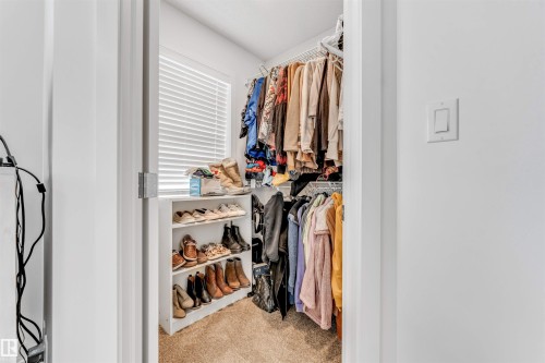 Walk-in closet featuring carpet flooring, a window with horizontal blinds, built-in wire shelving, and a shoe rack - 116 3305 Orchards Link Sw, Edmonton, AB 