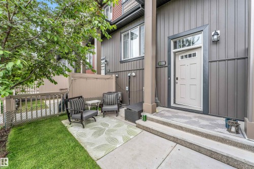 Vertical siding exterior with a light-colored entry door, featuring a transom window and integrated lighting - 116 3305 Orchards Link Sw, Edmonton, AB 