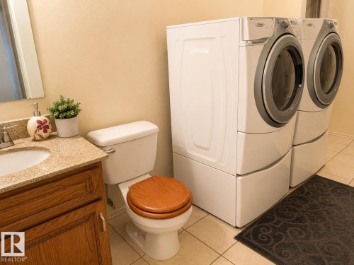 Bathroom featuring a vanity with a light-colored countertop and integrated sink, wood-finish cabinetry, a toilet with a wood-finish seat, and light-toned tile flooring - 1 Munro Court, Leduc, AB 