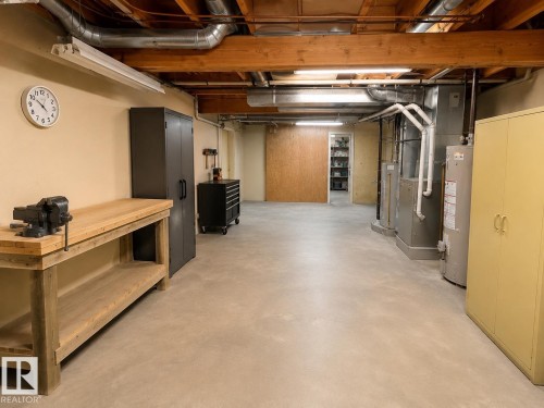 Spacious utility area featuring exposed wood beam ceiling, concrete flooring, and a built-in workbench with storage shelving - 1 Munro Court, Leduc, AB 