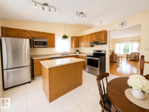 Kitchen featuring wood cabinetry, stainless steel appliances, a center island with a light-toned countertop, and light-toned tile flooring - 1 Munro Court, Leduc, AB 