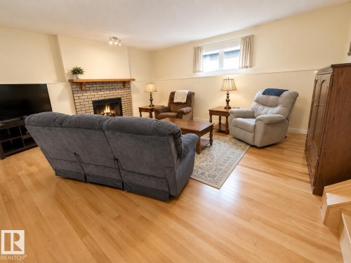 Living area featuring wood-finish flooring, a brick fireplace with a wood mantel, and track lighting - 1 Munro Court, Leduc, AB 