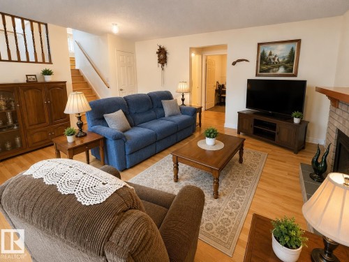 Bright living area featuring wood-finish flooring, a brick fireplace with a wood mantel, and warm neutral wall tones - 1 Munro Court, Leduc, AB 