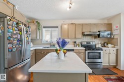 Kitchen featuring a center island with a white countertop, beige cabinetry, stainless steel appliances, and a window above the sink - 