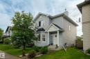 Two-story residence featuring light gray siding with white trim, a covered entry porch supported by white columns, a bay window, and an established front yard with a mature tree - 220 85St, Edmonton, AB 