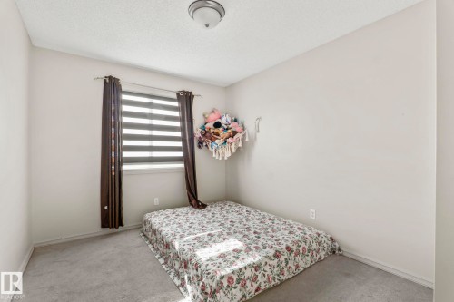 Carpeted room featuring a window with horizontal blinds and full-length curtains, neutral wall tones, and a ceiling-mounted light fixture - 220 85St, Edmonton, AB 