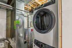 Stacked front-load washer and dryer units, visible mechanicals including a water heater, and a furnace unit - 