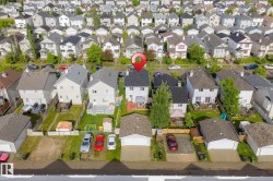 Aerial view of a residential property featuring a white two-story home with a dark shingle roof and a rear deck - 