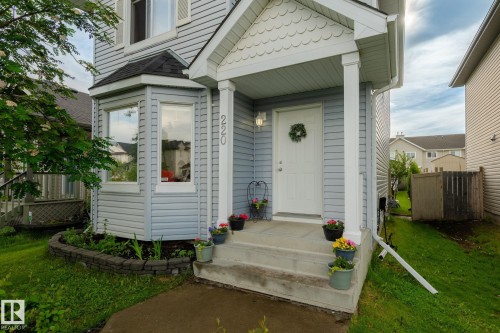 Residential facade featuring light blue horizontal siding, a covered front porch with white columns, and a bay window with a dark roofline - 220 85St, Edmonton, AB 