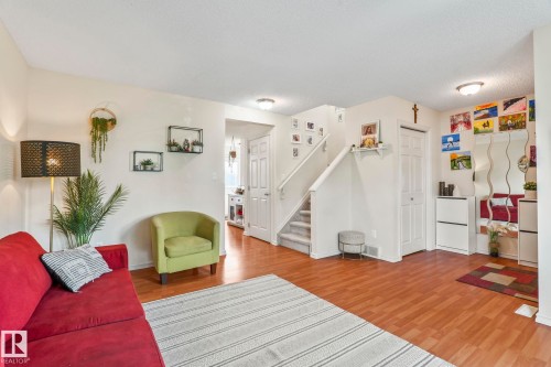 Open living space featuring wood-finish flooring, white walls, and a staircase with carpeted treads - 220 85St, Edmonton, AB 
