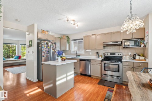 Open-concept kitchen featuring wood-finish flooring, stainless steel appliances, a center island with a white countertop, and recessed lighting - 220 85St, Edmonton, AB 