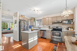 Open-concept kitchen featuring wood-finish flooring, stainless steel appliances, a center island with a white countertop, and recessed lighting - 