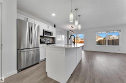 Modern kitchen featuring an expansive island with a matte black faucet, stainless steel appliances, white cabinetry, and a marble-finish backsplash - 
