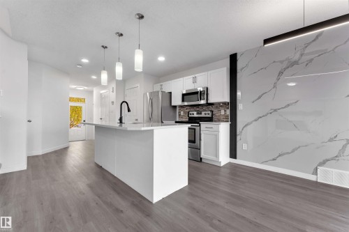 Modern kitchen featuring a central island with pendant lighting, stainless steel appliances, and wood-finish flooring - 5405 Crabapple Loop, Edmonton, AB 
