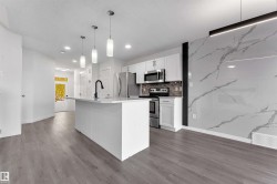 Modern kitchen featuring a central island with pendant lighting, stainless steel appliances, and wood-finish flooring - 