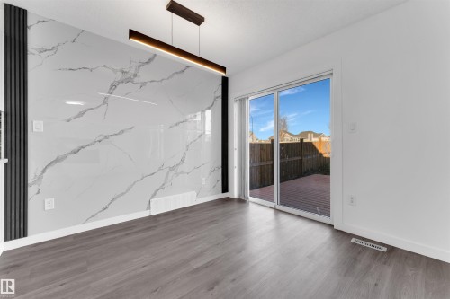 Feature wall with marble-look paneling, wood-finish flooring, and a modern linear pendant light fixture - 5405 Crabapple Loop, Edmonton, AB 