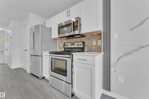 Kitchen featuring white cabinetry, stainless steel appliances, a mosaic tile backsplash, and light wood-finish flooring - 5405 Crabapple Loop, Edmonton, AB 