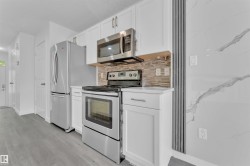 Kitchen featuring white cabinetry, stainless steel appliances, a mosaic tile backsplash, and light wood-finish flooring - 