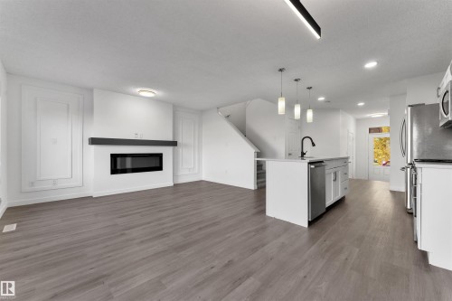 Open-concept living space featuring wood-finish flooring, a contemporary linear fireplace with a dark mantel, and panel wall detailing - 5405 Crabapple Loop, Edmonton, AB 