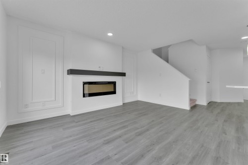 Open concept living space featuring wood-finish flooring, a linear electric fireplace with a dark mantel, recessed lighting, and a paneled accent wall - 5405 Crabapple Loop, Edmonton, AB 