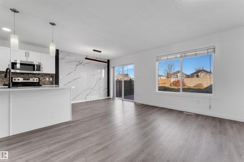 Open concept living area featuring wood-finish flooring, white walls, and a large window - 5405 Crabapple Loop, Edmonton, AB 