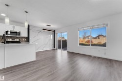 Open concept living area featuring wood-finish flooring, white walls, and a large window - 