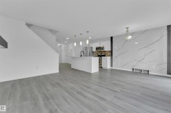 Open-concept living area featuring light wood-finish flooring, a contemporary kitchen with stainless steel appliances, a center island with pendant lighting, and a striking accent wall with a marble-effect finish - 