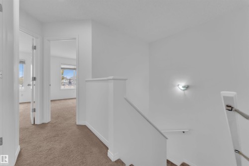 Upper level landing featuring carpeted flooring, white painted walls, a half-wall railing, and a wall-mounted sconce - 5405 Crabapple Loop, Edmonton, AB 