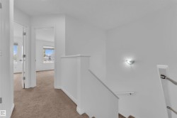 Upper level landing featuring carpeted flooring, white painted walls, a half-wall railing, and a wall-mounted sconce - 