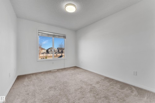 Bright interior space featuring a large window with horizontal blinds, neutral-toned carpet flooring, white walls, and a ceiling-mounted light fixture - 5405 Crabapple Loop, Edmonton, AB 