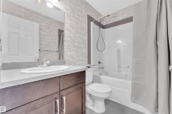 Bathroom featuring a dark wood-finish vanity with an undermount sink, a light-colored countertop, and a full-width mirror - 