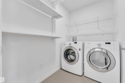 Laundry area featuring a side-by-side washer and dryer, tile flooring, and white wall shelving - 