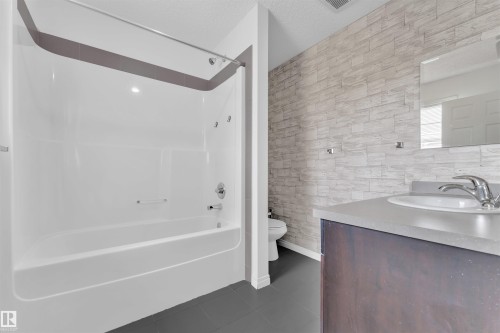Bathroom featuring a white tub-shower combination with chrome fixtures, a dark wood-finish vanity with a light countertop, an integrated sink, and a framed mirror - 5405 Crabapple Loop, Edmonton, AB 