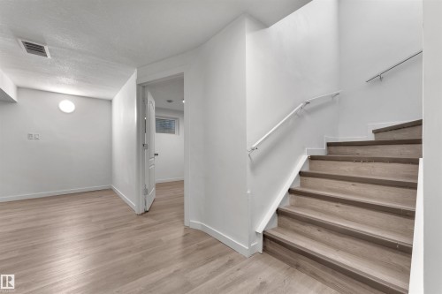 Interior staircase featuring wood-finish treads and risers, complemented by a white handrail and a metal wall-mounted railing - 5405 Crabapple Loop, Edmonton, AB 