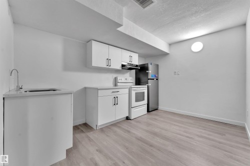 Compact kitchen area featuring white cabinetry, light-toned countertops, and wood-finish flooring - 5405 Crabapple Loop, Edmonton, AB 