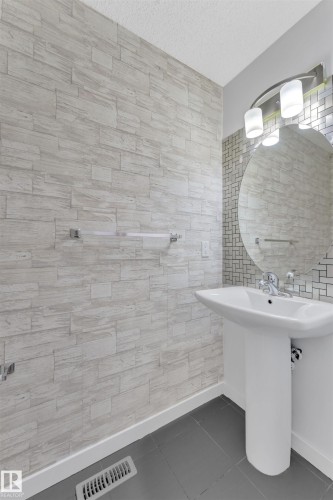 Pedestal sink with chrome fixtures, a circular mirror, and a contemporary vanity light - 5405 Crabapple Loop, Edmonton, AB 