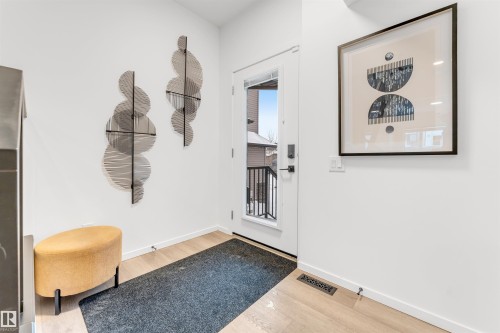 Bright entryway featuring a full-light exterior door with black hardware, light wood-finish flooring, and crisp white walls - 6203 47 Avenue, Beaumont, AB 