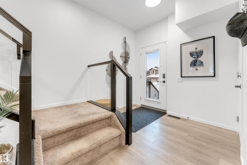 Entryway featuring a contemporary glass and dark metal railing, light wood-finish flooring, and a white paneled entry door - 6203 47 Avenue, Beaumont, AB 